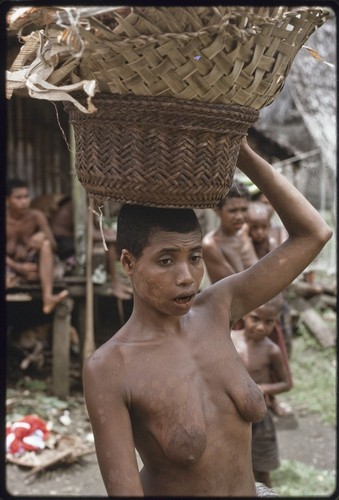 Mortuary ceremony: woman carries baskets partially filled with fiber skirts and banana leaf bundles