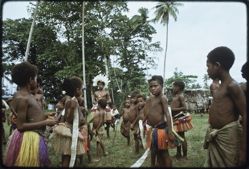 Dance: children wear short fiber skirts and carry flattened pandanus leaves for circle dance, younger children look on