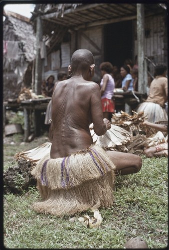 Mortuary ceremony: mourning woman with shaved head and wearing two-tiered fiber skirt, arranges banana leaf bundles at exchange