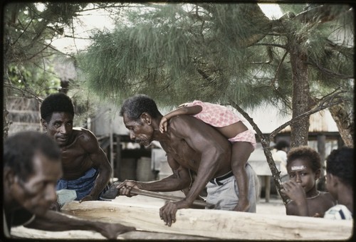 Manus: men building a canoe, small child on one man's back, Pere village