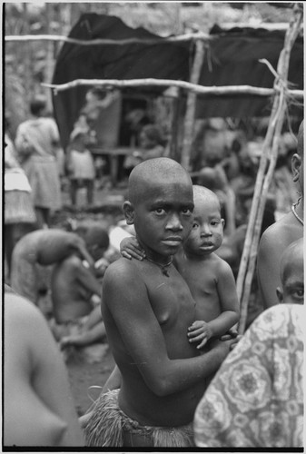 Mortuary ceremony, Omarakana: mourning girl, her face and body blackened with ash and her head shaved, carries infant