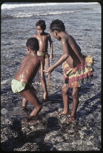 Fishing: children play with net in shallow lagoon near Wawela village, boys wear leaf coverings, girl (r) wears short fiber skit