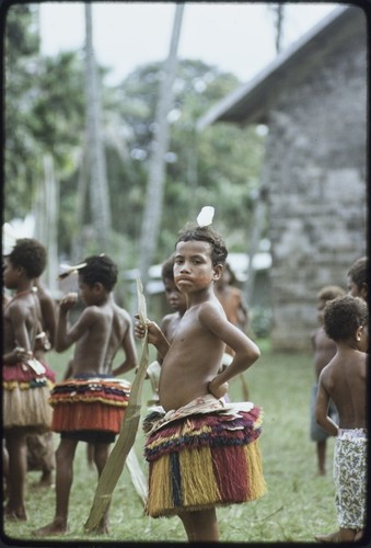 Dance: children wear colorful fiber skirts and carry pandanus leaves, girl (center) wears paint on face