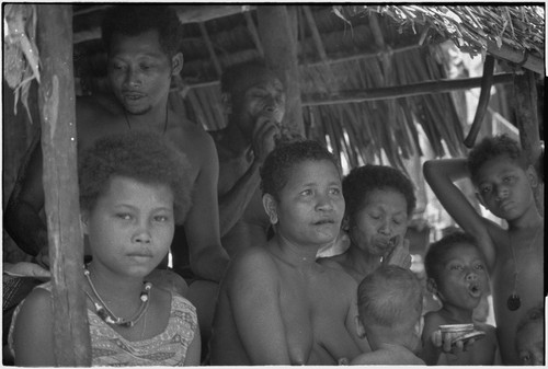 People smoke and chew betel nut, in shade under the awning of a shelter