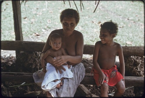 Woman holds infant, child sits next to them