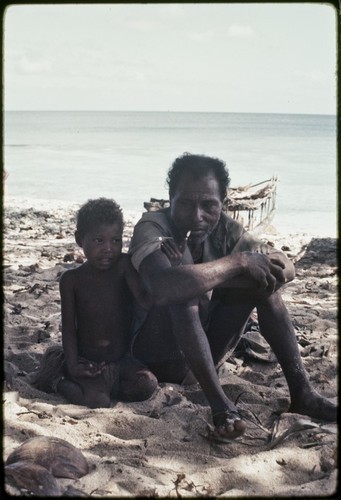 Smoking man sits with young girl on a beach near Kaibola village