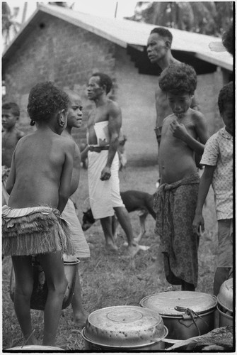 Mortuary ceremony: children stand next to smoked fish and tin pots filled with food to be shared with mourners