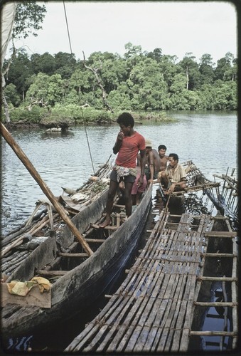 Fishing: man on canoe (center) displays fish on outrigger platform, fish will be given in exchanges or bartered