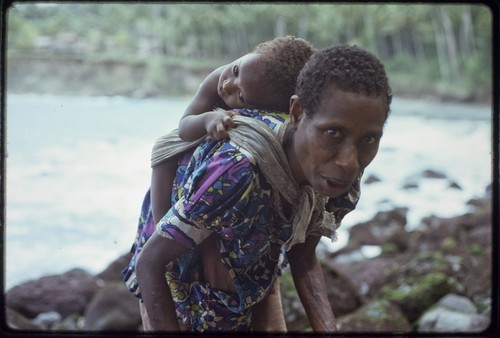 Kairiru: on rocky coastline, woman with small child in a sling on her back