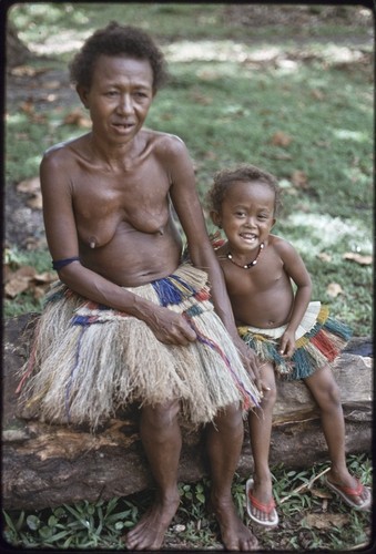 Mogiovyeka's wife and daughter, Imala, wearing fiber skirts, girl wears shell necklace