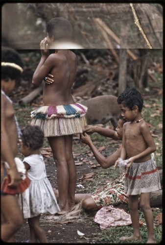 Seated woman adjusts short banana fiber skirt worn by a an adolescent girl