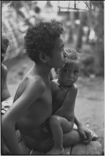 Boy holds a baby who looks at the camera with doubtful expression