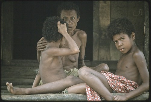 Boys on house veranda, woman sits close by