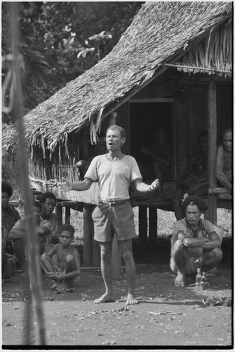 Meeting: man speaks in front of gathered crowd, gestures with his arms