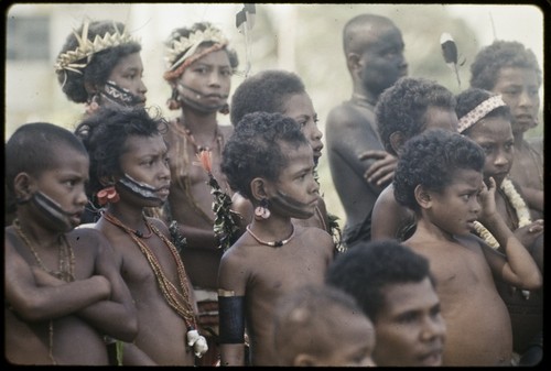 Dance: children with painted faces and shell necklaces observe a dance