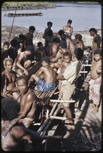 Canoe-building: people gathered for dedication of new canoe, men making adjustments to sides of canoe