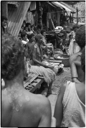 Mortuary ceremony: woman (center) holds banana leaf bundles for ritual exchange, large basket (r)