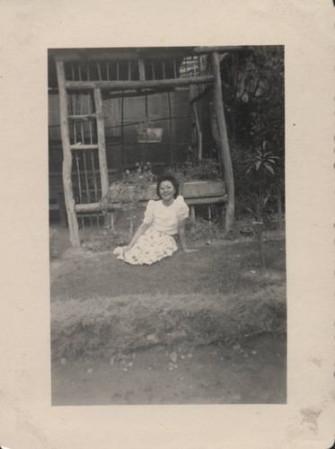 Young woman sits in front of wooden garden bower at Poston incarceration camp