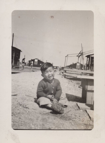 Boy with muddy shoes sitting on ground at Poston incarceration camp