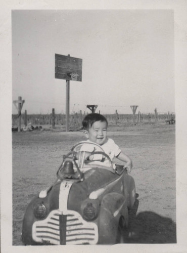 Little boy in toy car with bell on hood at Poston incarceration camp