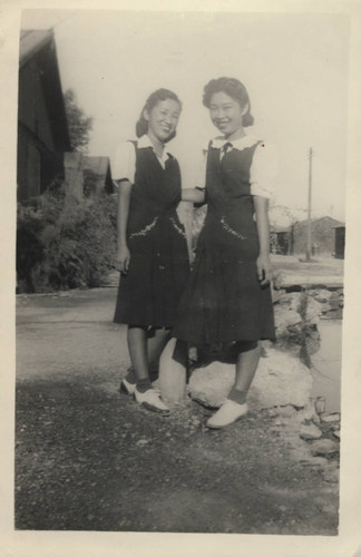 Two young women stand together in front of the barracks at Poston incarceration camp