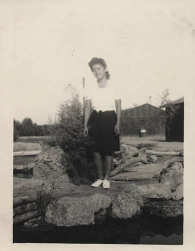 Young woman stands on path in front of a pond at Poston incarceration camp