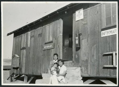 Photograph of two women an a young child posing in front of the infirmary at Cow Creek Camp in Death Valley