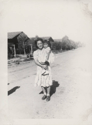 Woman in flowered dress holds small child at Poston incarceration camp