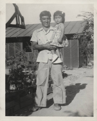 Man holds toddler in sundress at Poston incarceration camp