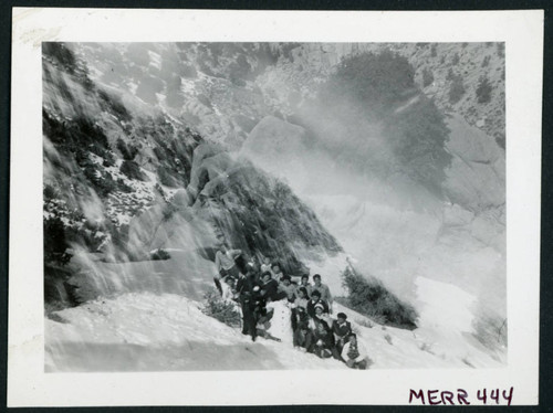 Photograph of a group of people holding snow balls on the side of a mountain with a snowman