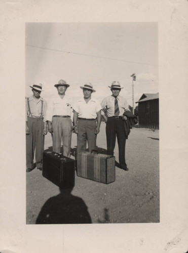 Men wearing hats and suitcases at Poston incarceration camp