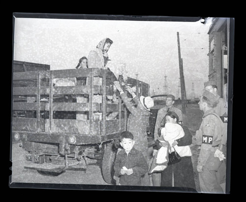 Japanese American family from Terminal Island unloading from the bed of a truck as military police watch on