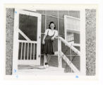 Sumi Seki wears a white shirt and plaid skirt while standing in front of barracks