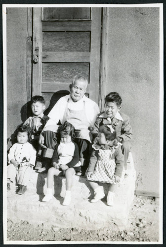 Photograph of Grandpa Tayama surrounded by five children in front of a door in Cow Creek Camp in Death Valley