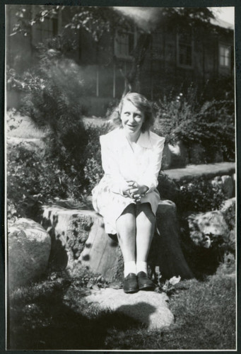 Photograph of Dr. Agnes V. Barlett sitting on a rock in front of the Manzanar hospital