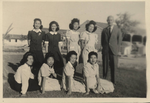 Man and young women sitting and standing on a lawn