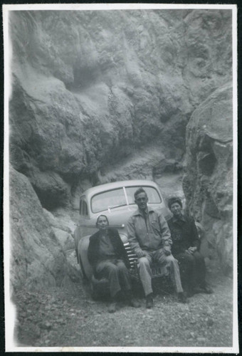 Photograph of three people sitting on a bumper in a canyon in Death Valley