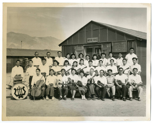 Photograph of a musical group at Manzanar posed in front of the Music Hall at Block 24