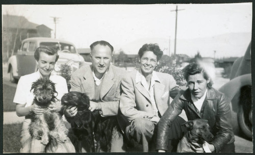 Photograph of people with dogs in front of a car and barracks