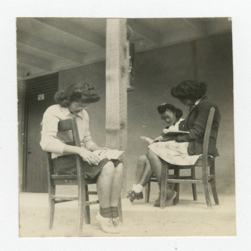 Nisei women reading outside barrack