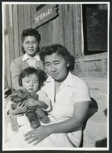 Photograph of two women an a young child posing in front of the infirmary at Cow Creek Camp in Death Valley