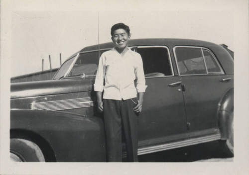 Young man stands in front of a car at Poston incarceration camp