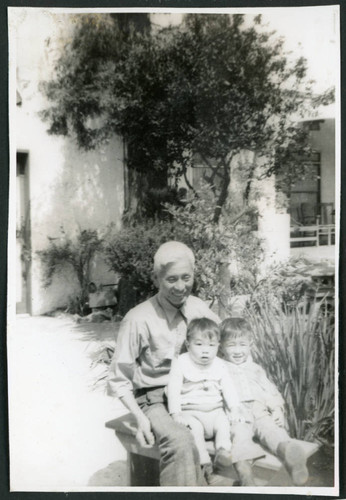 Photograph of Ned Morioka with his grandfather and cousin sitting on a bench with a house in the background