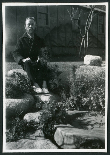 Photograph of a man in a robe sitting on a rock wall in front of the Manzanar hospital