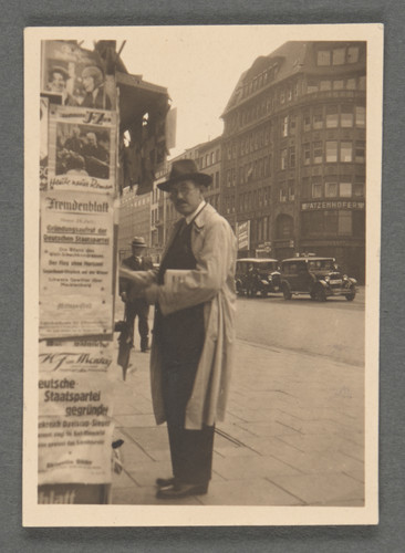 [Otto Stern by newspaper stand on city street.]