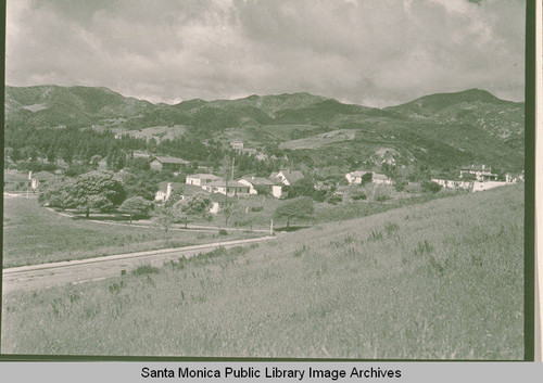 View of an open field and houses looking up Temescal Canyon and Radcliffe Avenue with the Santa Monica Mountains in the background