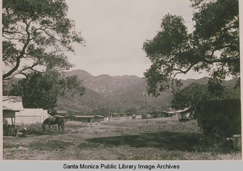 Early settlement of Founder's Oak Island in Temescal Canyon showing tents, an early car, and grazing horse in the foreground