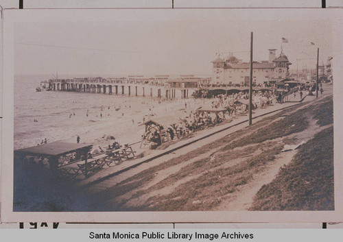 Long Beach, Calif. crowds gather for picnicking and other recreation showing the pier in the distance and a railroad runs by the beach