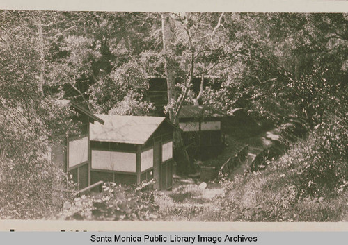 Casitas are in view among the oak trees by a Craftsman bridge at Assembly Camp, Temescal Canyon, Calif