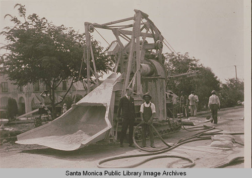 Workers standing around a curbmaking machine by Village Green in Huntington Palisades, Calif